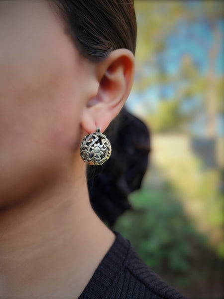 Model is wearing 925 Sterling silver ball hoop earrings with a delicate floral design. The earrings are made of a filigree pattern and have oxidised finish.