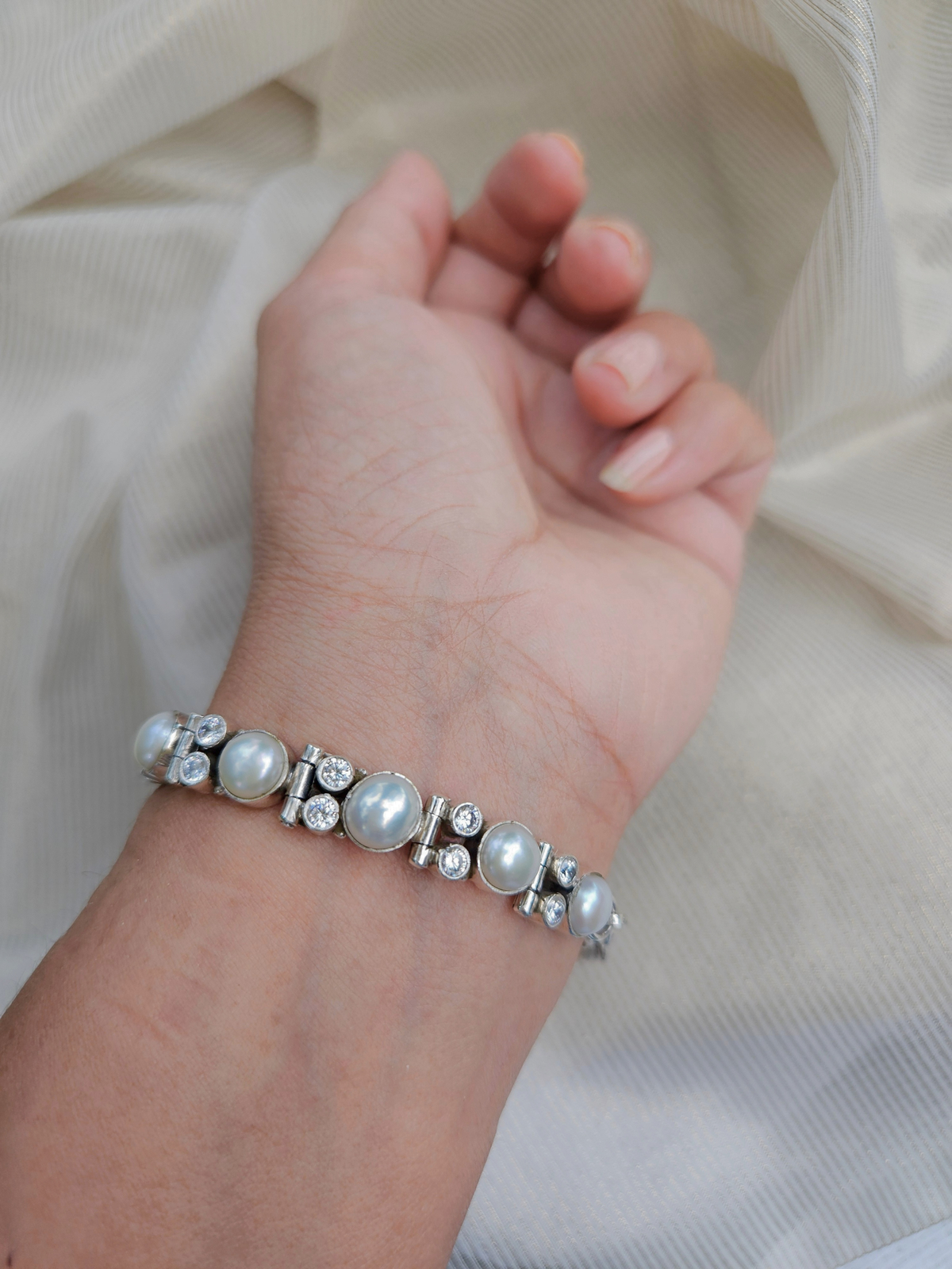 “Handmade 925 sterling silver bracelet with white pearls and cubic zirconia, worn on the wrist against ivory fabric”