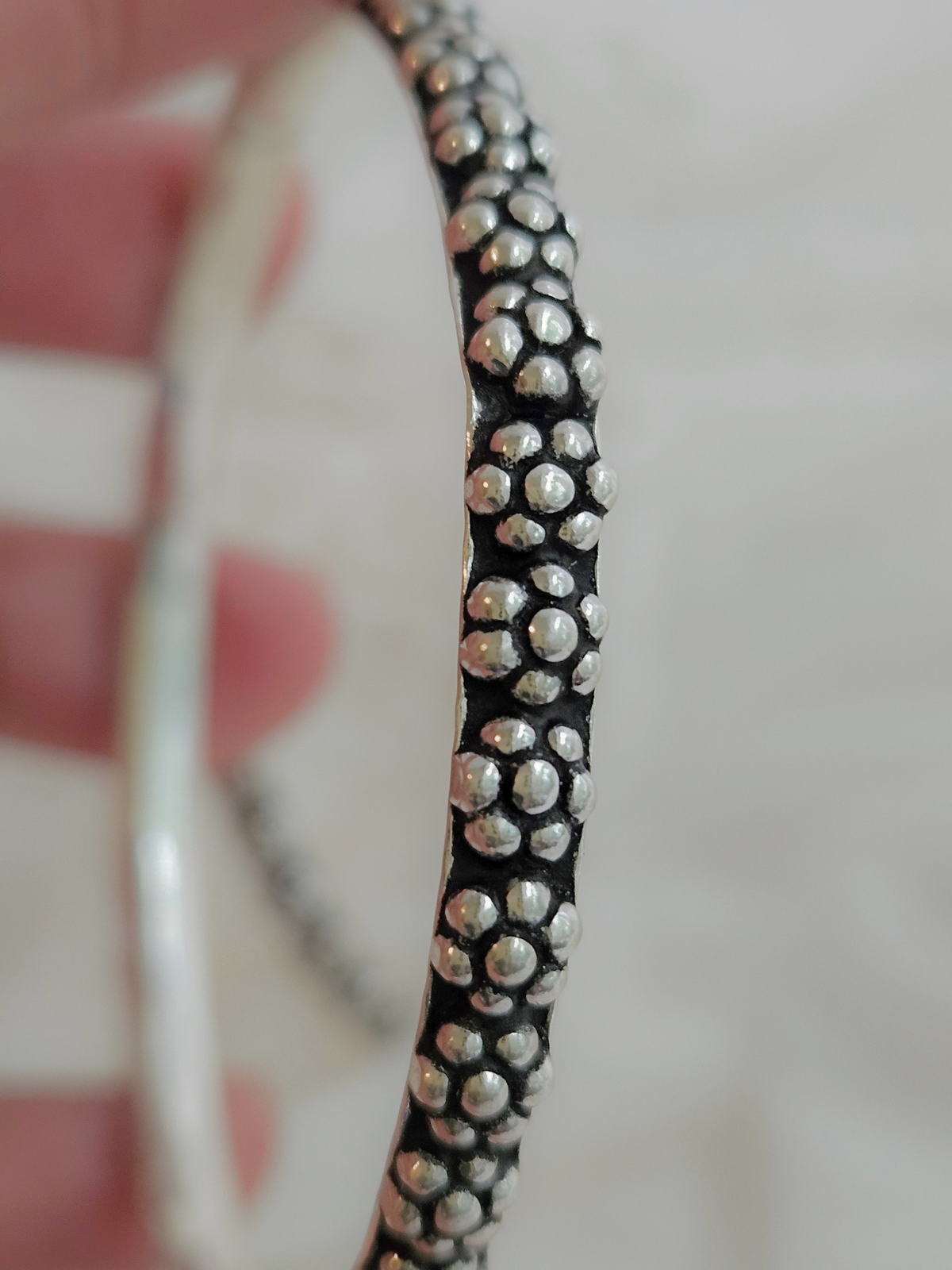 Oxidized 925 sterling silver bangle with raised floral dot clusters and a wavy edge, shown up close in hand