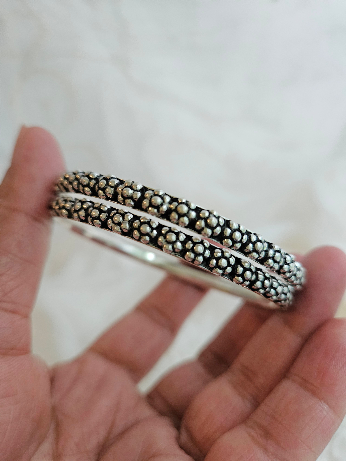 Oxidized 925 sterling silver bangle with raised floral dot clusters and a wavy edge, shown up close in hand