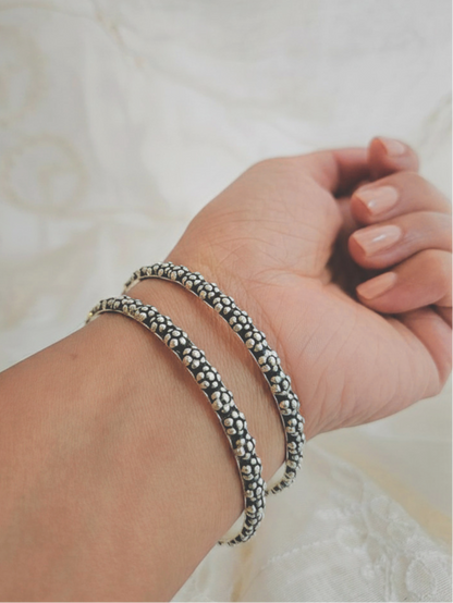 Oxidized 925 sterling silver bangle with raised floral dot clusters and a wavy edge, shown up close in hand