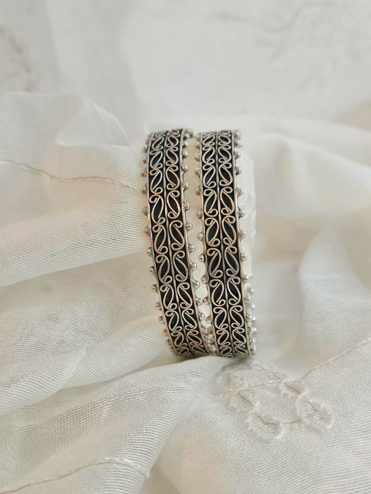 Pair of oxidized pure silver bangles with paisley filigree scrollwork and beaded edges on ivory fabric made in jaipur by hand