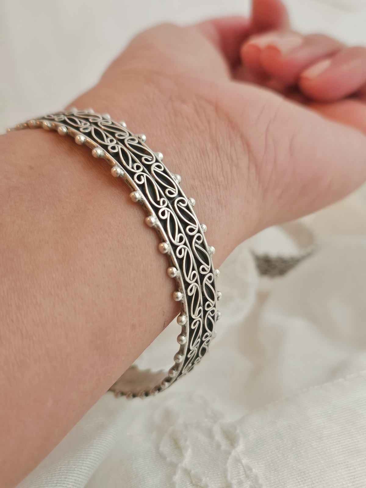 Pair of oxidized silver bangles with paisley filigree scrollwork and beaded edges on ivory fabric