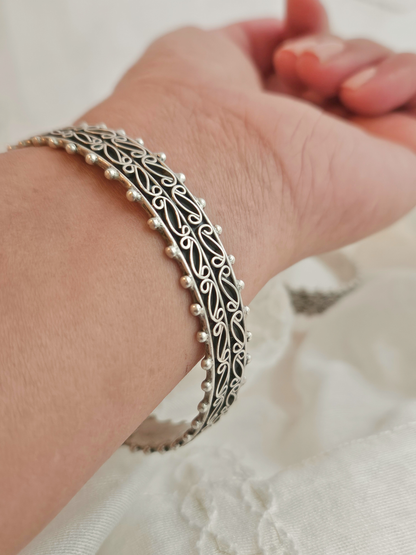 Pair of oxidized silver bangles with paisley filigree scrollwork and beaded edges on ivory fabric