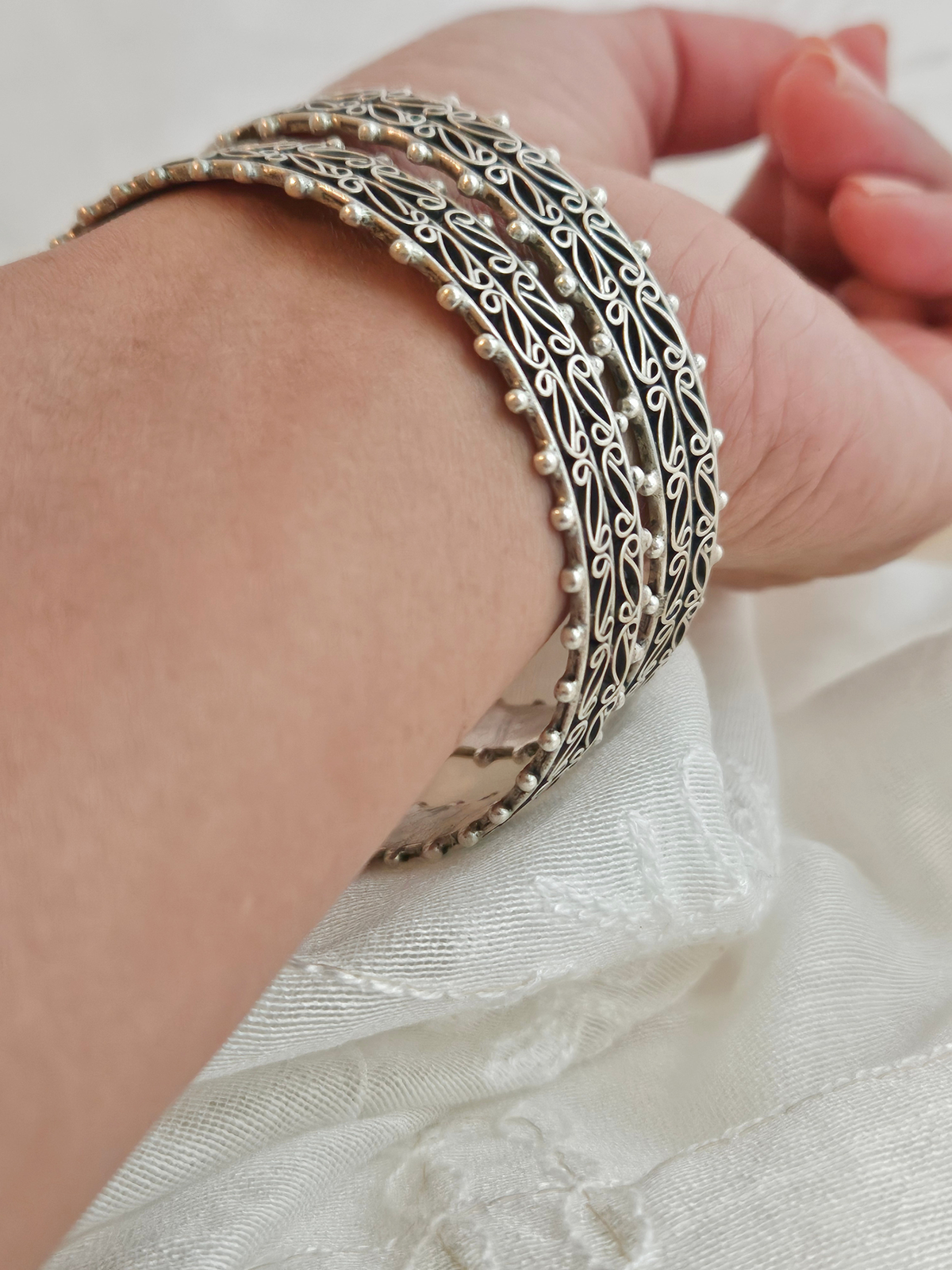 Pair of oxidized 925 Sterling Silver silver bangles with paisley filigree scrollwork and beaded edges on ivory fabric