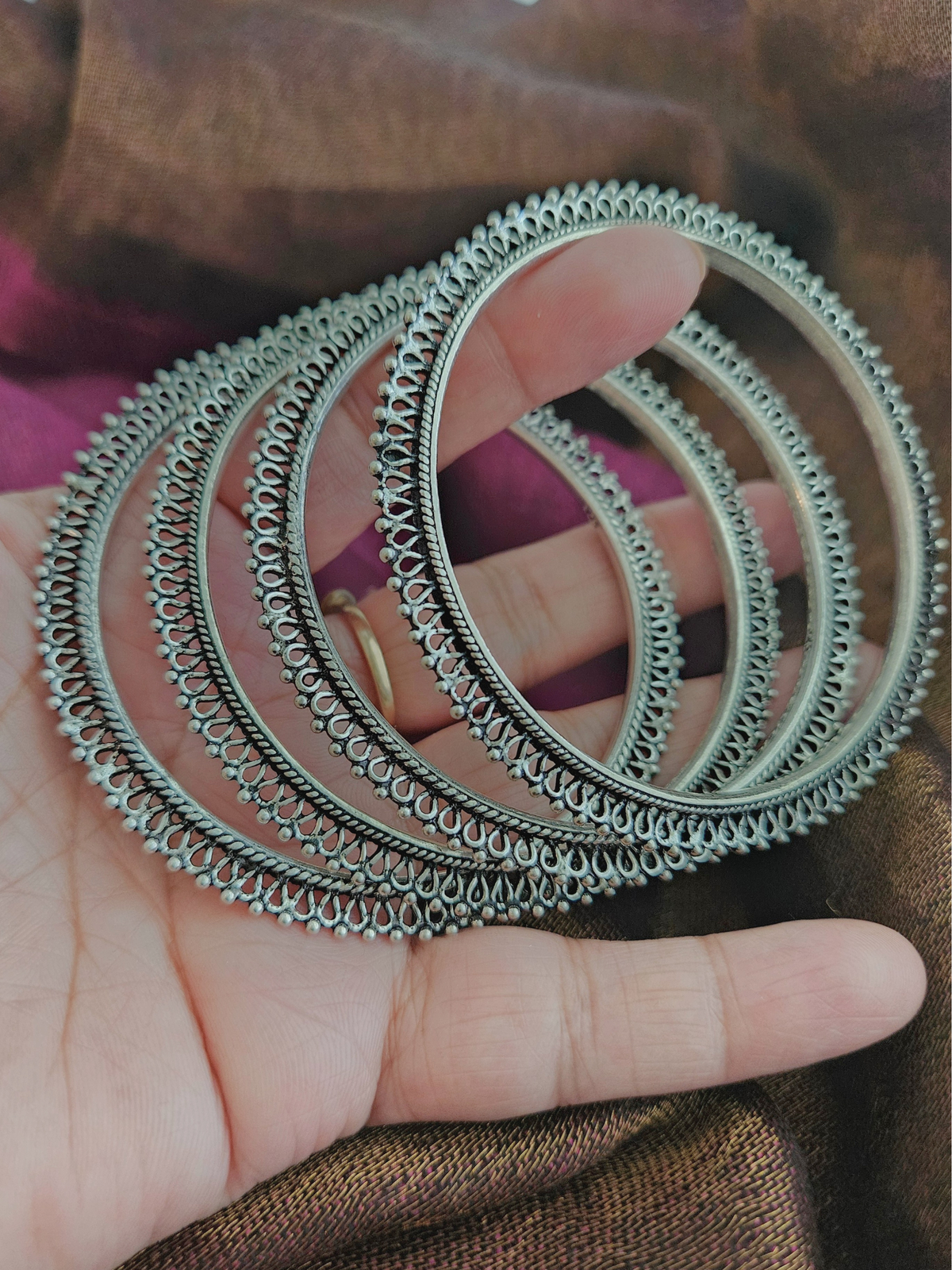 Stack of oxidized silver bangles with beaded edges and twisted rope detailing on a wrist against a magenta silk saree
