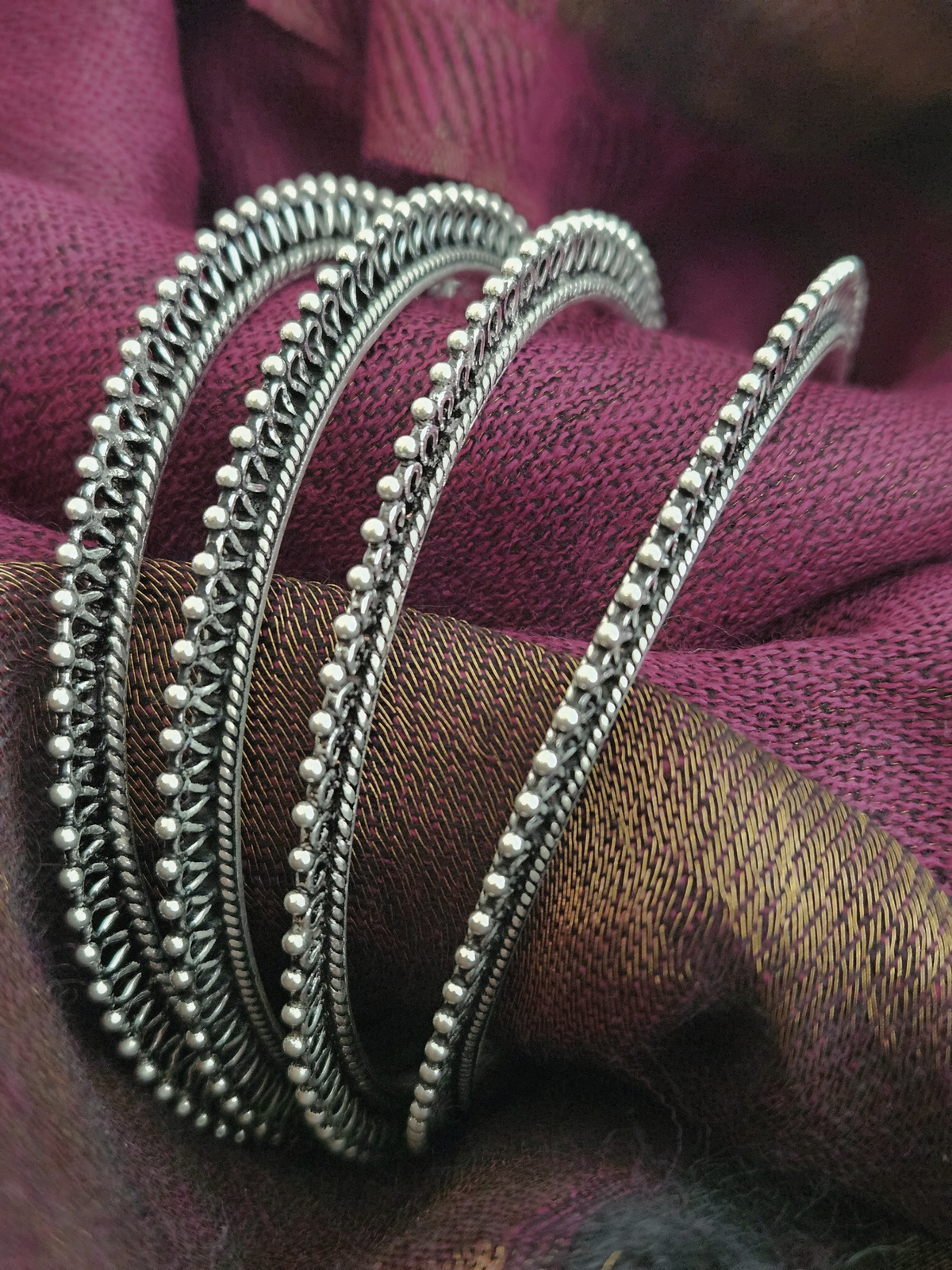 Stack of oxidized silver bangles with beaded edges and twisted rope detailing on a wrist against a magenta silk saree