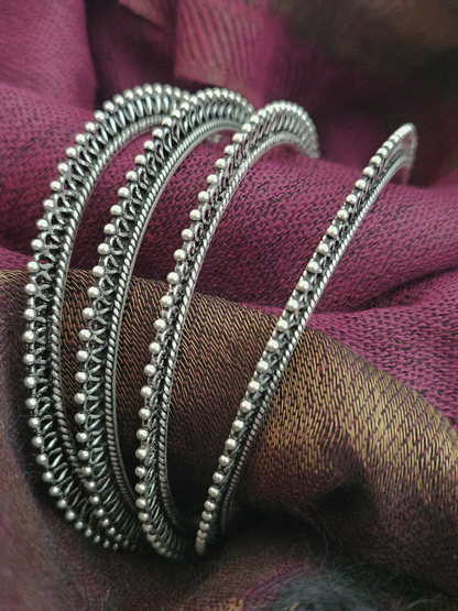 Stack of oxidized silver bangles with beaded edges and twisted rope detailing on a wrist against a magenta silk saree