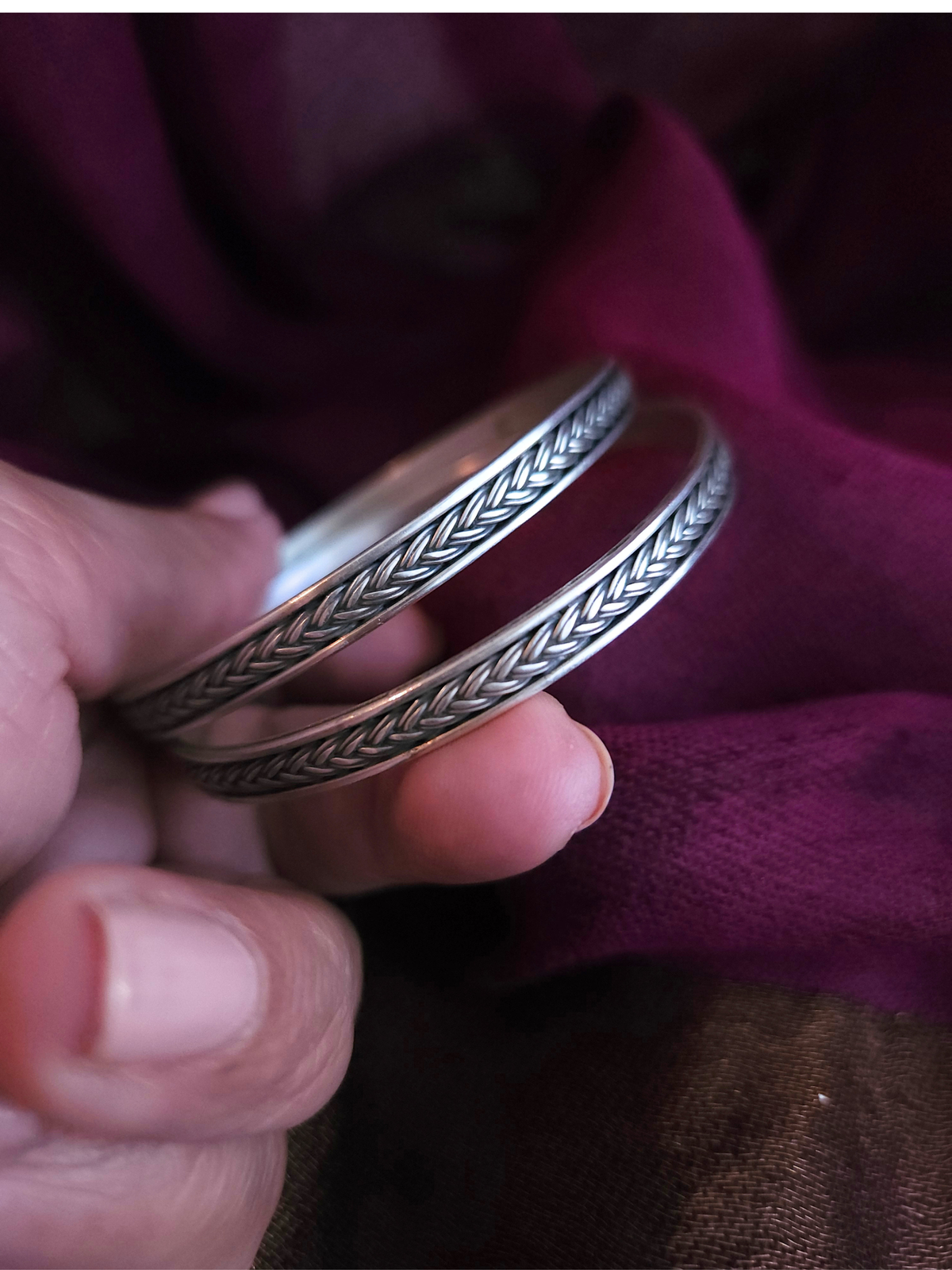 Two oxidized 925 sterling silver braided bangles with polished rims on a wrist against a plum silk saree