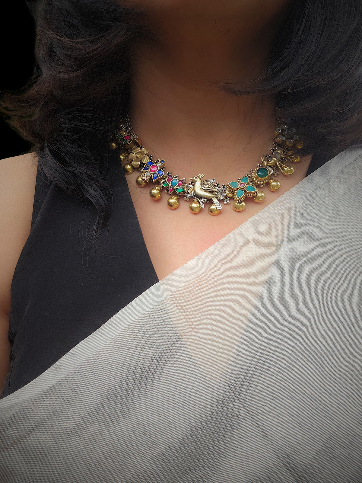 Woman wearing a dual-tone silver kundan charm necklace with a black blouse and an ivory handloom saree
