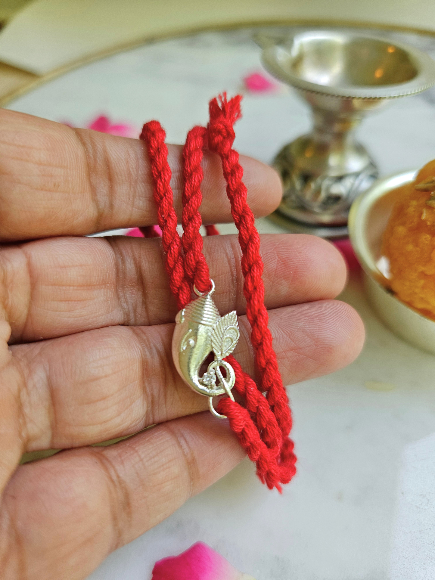 Silver Ganesha rakhi held in hand showing charm size