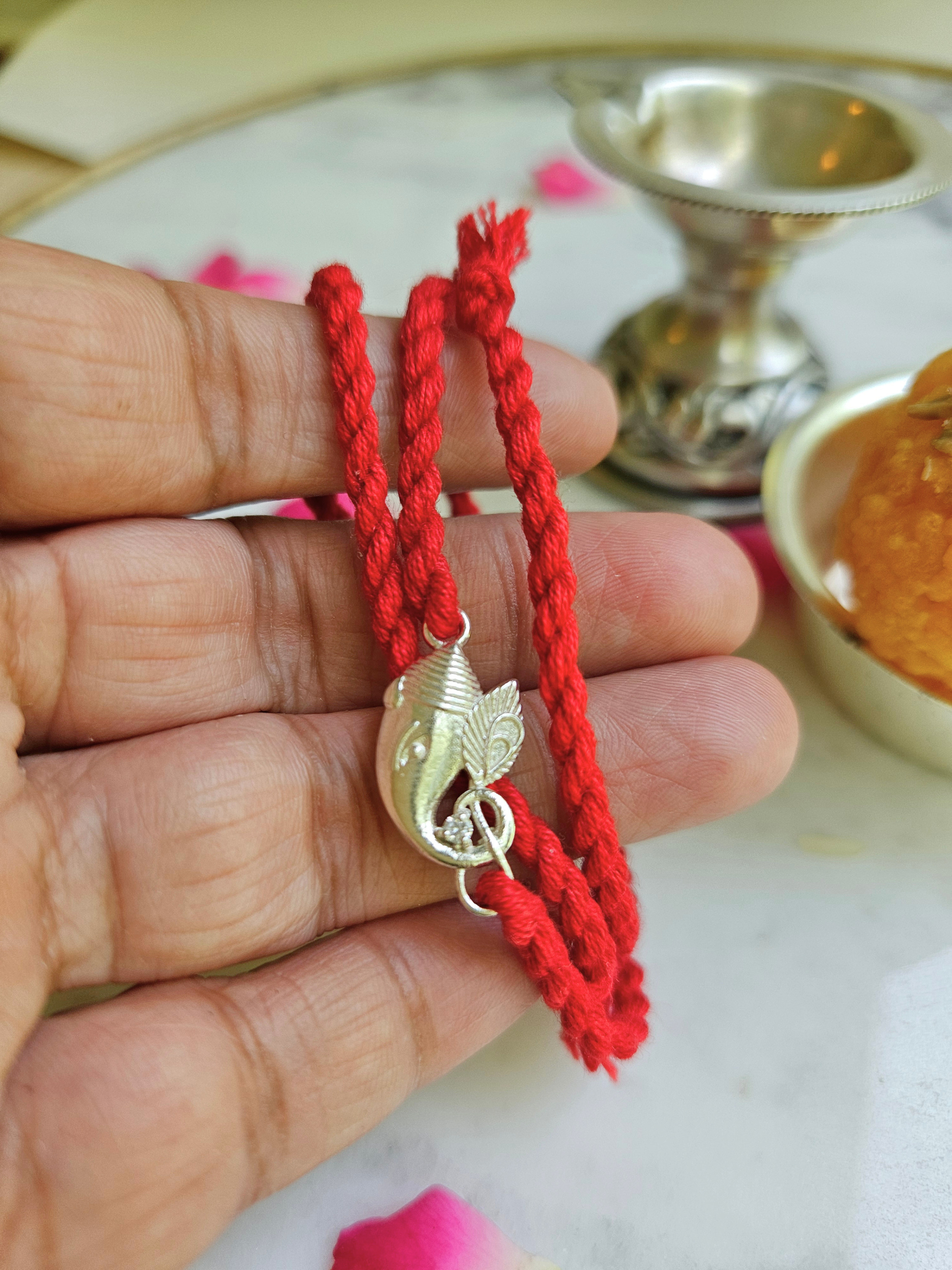 Silver Ganesha rakhi held in hand showing charm size