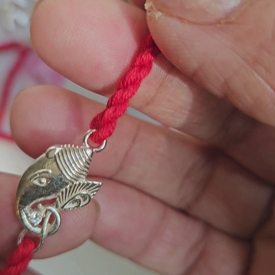 Silver Ganesha rakhi held in hand showing charm size