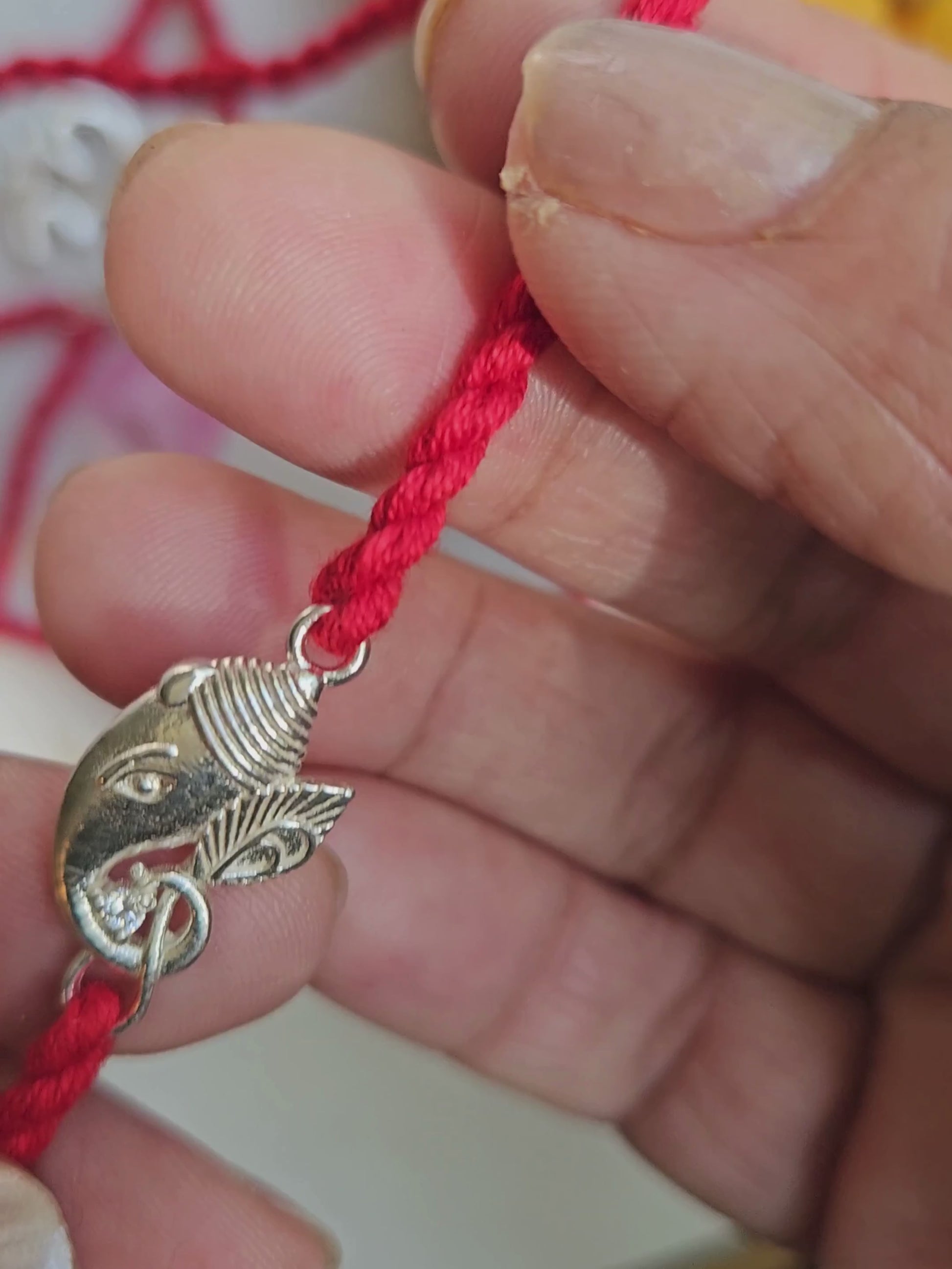 Silver Ganesha rakhi held in hand showing charm size