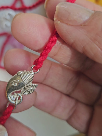 Silver Ganesha rakhi held in hand showing charm size